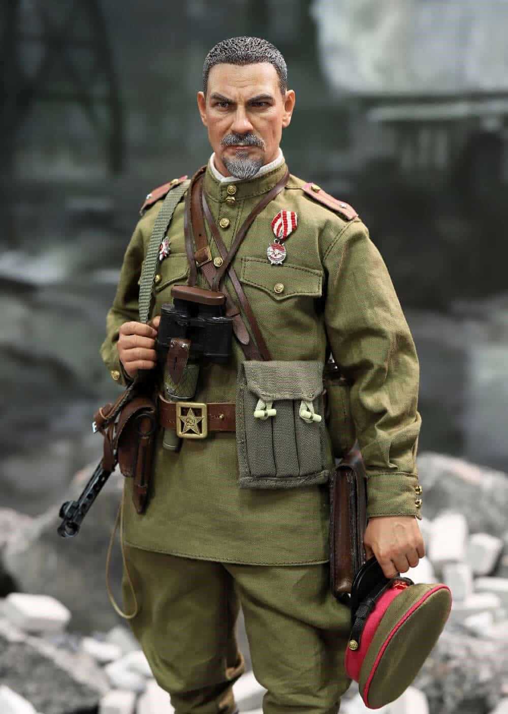  壁紙 — 一個穿著橄欖綠軍裝的詳細軍事人偶站在瓦礫中，手持望遠鏡和帽子。