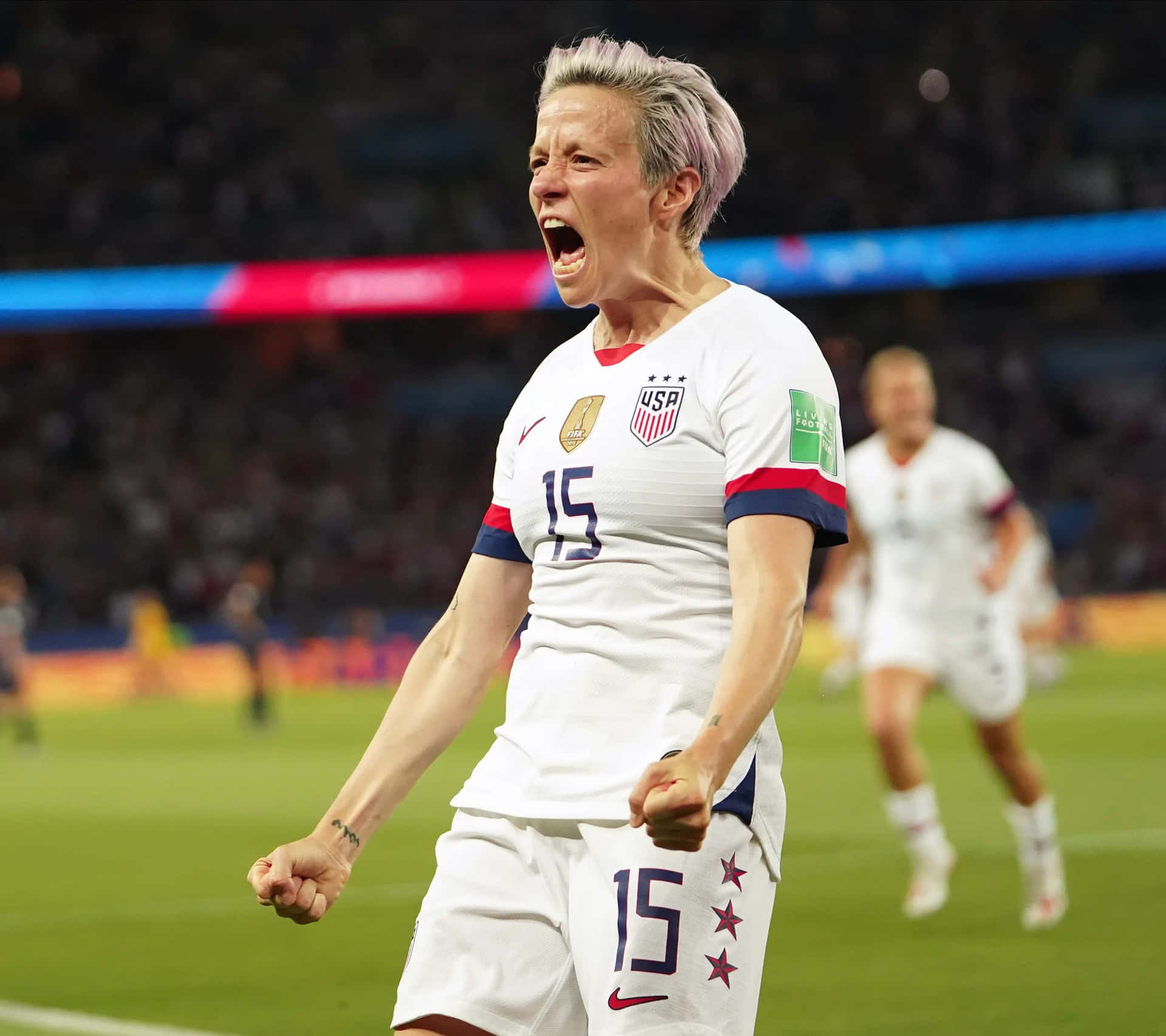  壁紙 — 一位短紫髮女足球員在球場上穿著15號球衣，勝利地尖叫。