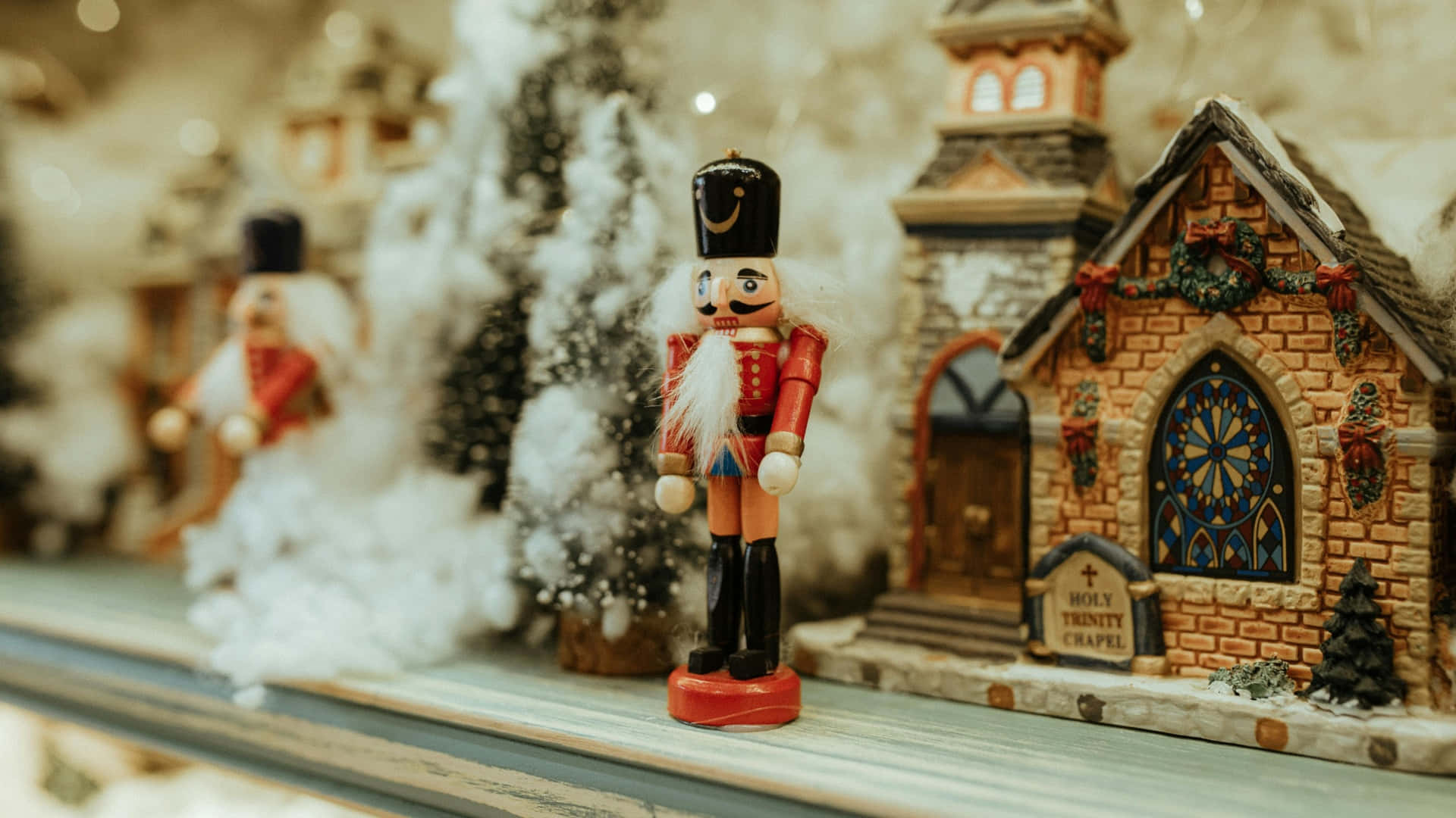  壁紙 — 一個節日氣氛的胡桃夾子士兵在一個裝飾著節日花環和雪的迷你聖三一小教堂旁站崗。