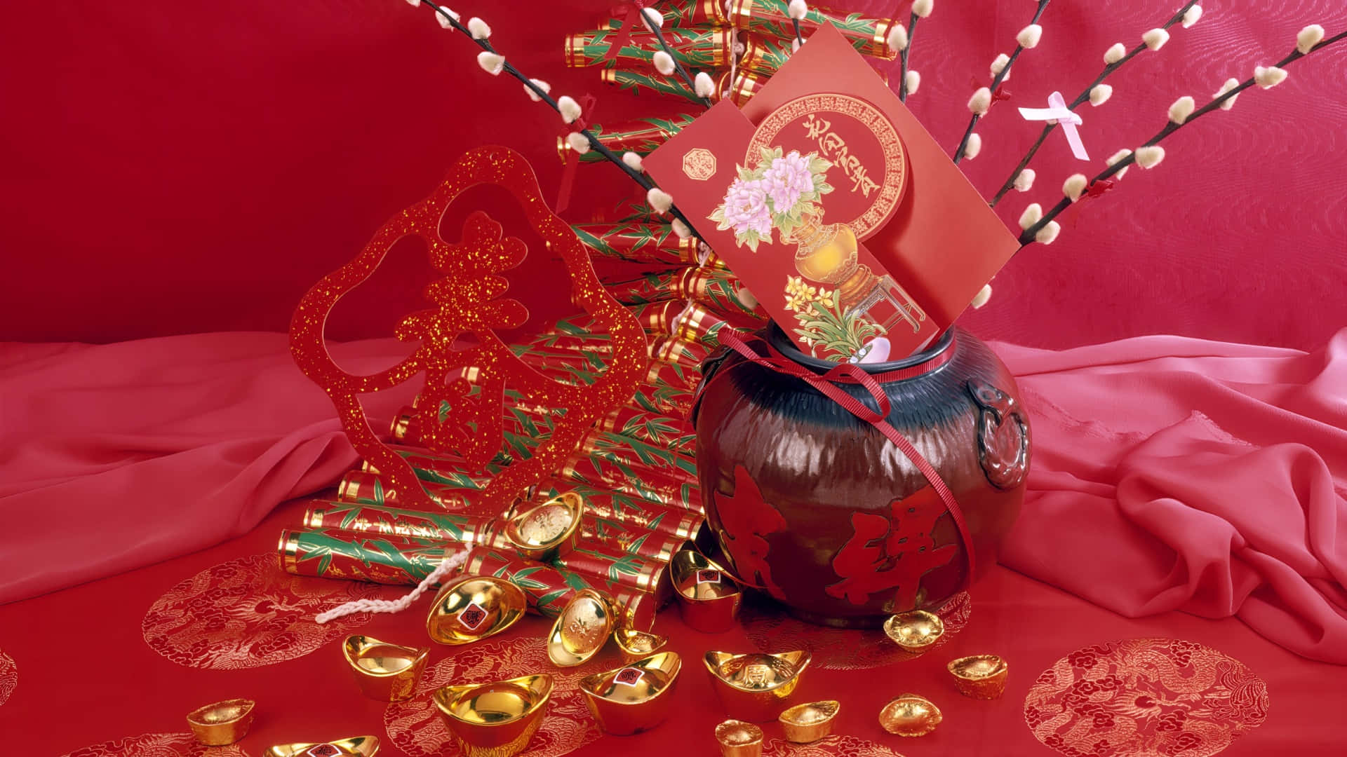  壁紙 — 一個節日紅色花瓶，飾有金錠和裝飾性樹枝，放在一塊濃郁的紅色布料上，周圍環繞著傳統的中國新年象徵物。