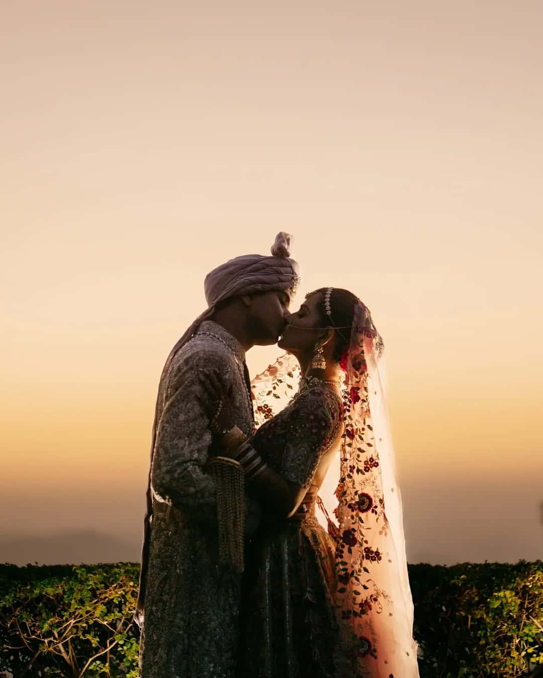 一對穿著傳統印度婚禮服飾的情侶在日落時分親吻