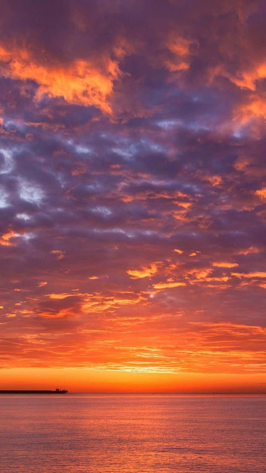 Sunset Photography 桌布 壁紙 — 熾熱的夕陽以鮮豔的橙色和紫色色調描繪天空，下方是平靜的海洋，遠處有船隻的剪影。