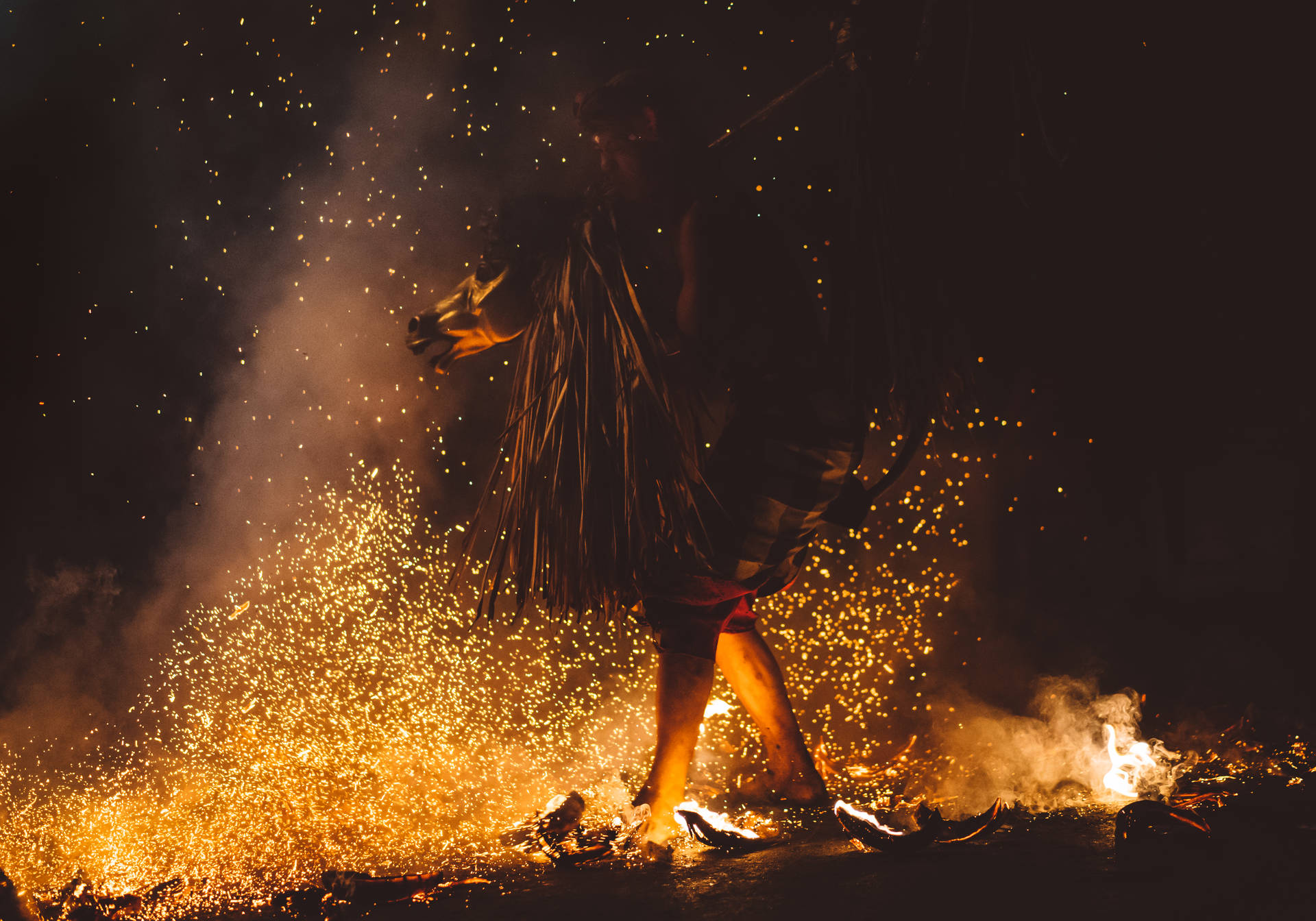 神秘月光女巫 壁紙 — 一個穿著草裙的人物在夜間於金色火花和煙霧中跳舞。