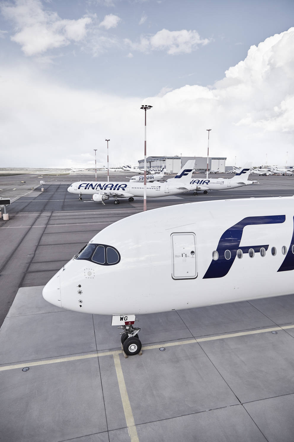 灰階芬蘭航空 壁紙 — 一架芬蘭航空飛機停在機場停機坪上，其他飛機和機庫在部分多雲的天空下。
