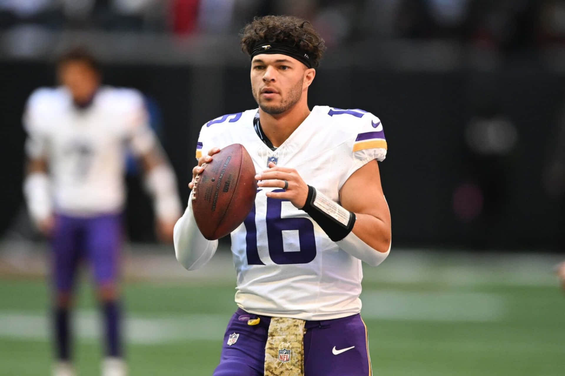 壁紙 — 一位專注的NFL四分衛身穿白色和紫色球衣，在比賽中持球準備傳球。