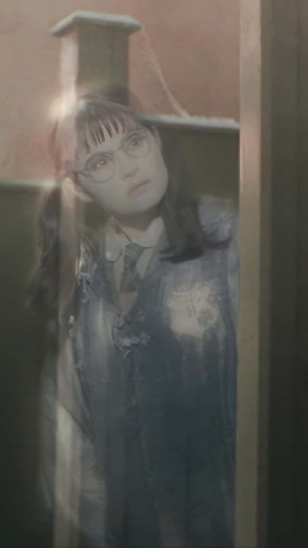  壁紙 — 一個穿著霍格華茲制服、幽靈般的女孩，帶著嚴肅的表情從木門框後窺視。