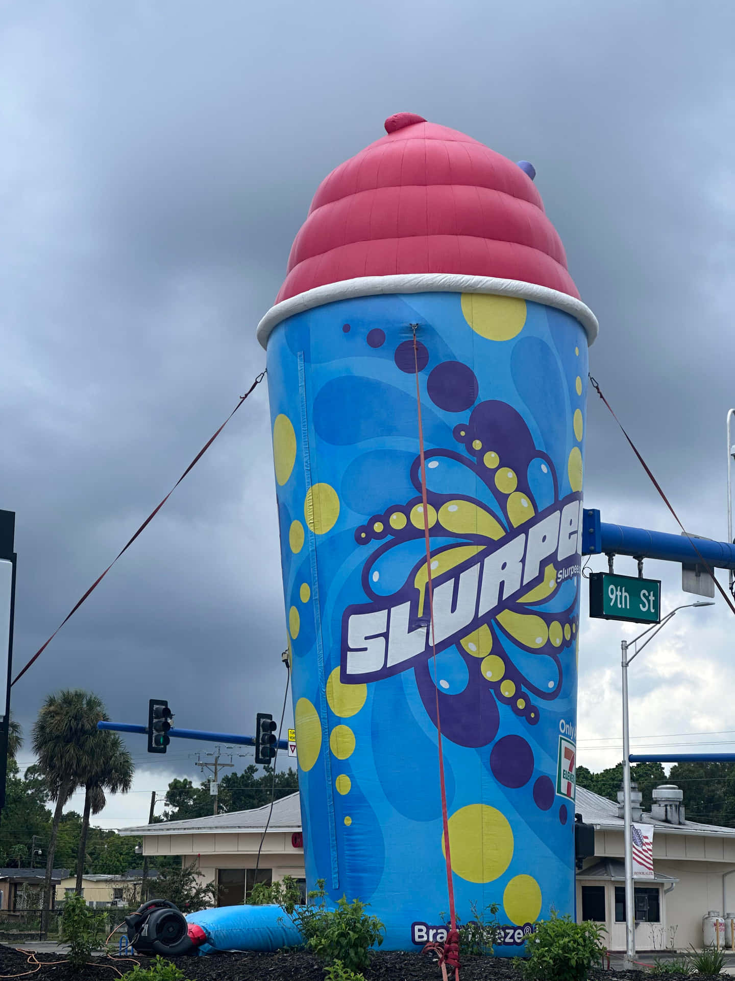 壁紙 — 一個巨大的充氣 Slurpee 杯雕塑在陰天下的街角聳立。