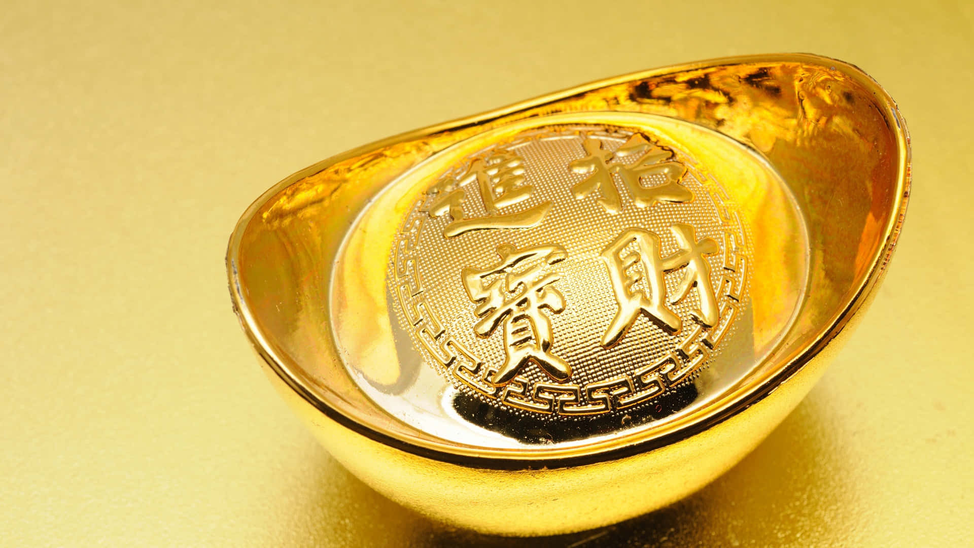  壁紙 — 閃閃發光的金條上刻有代表繁榮的中文字，放置在相配的金色表面上。
