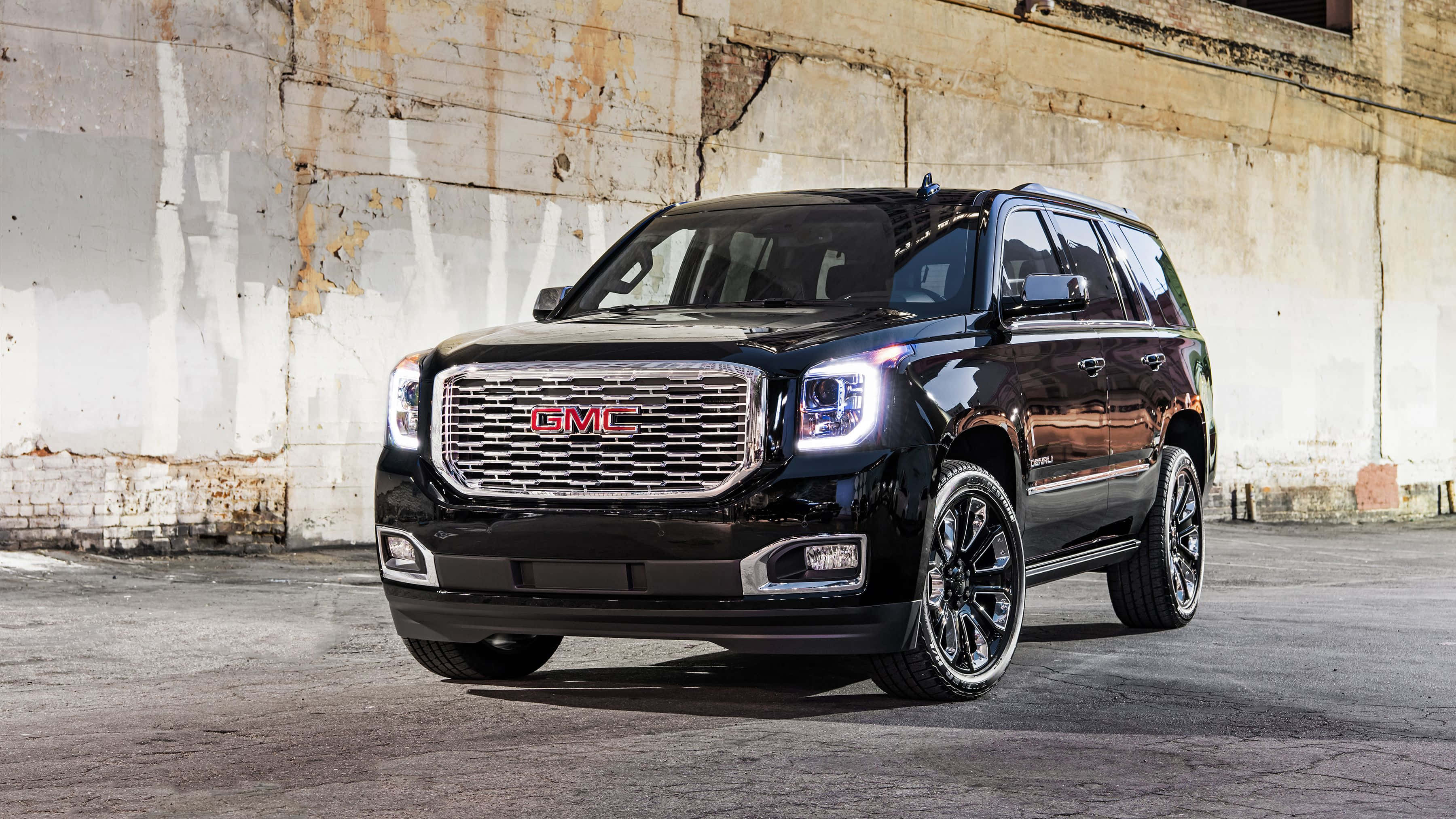 Gmc Yukon 桌布 壁紙 — 一輛光澤黑色GMC Yukon SUV，配備鍍鉻飾件和訂製輪圈，大膽地矗立在風化的混凝土牆前。