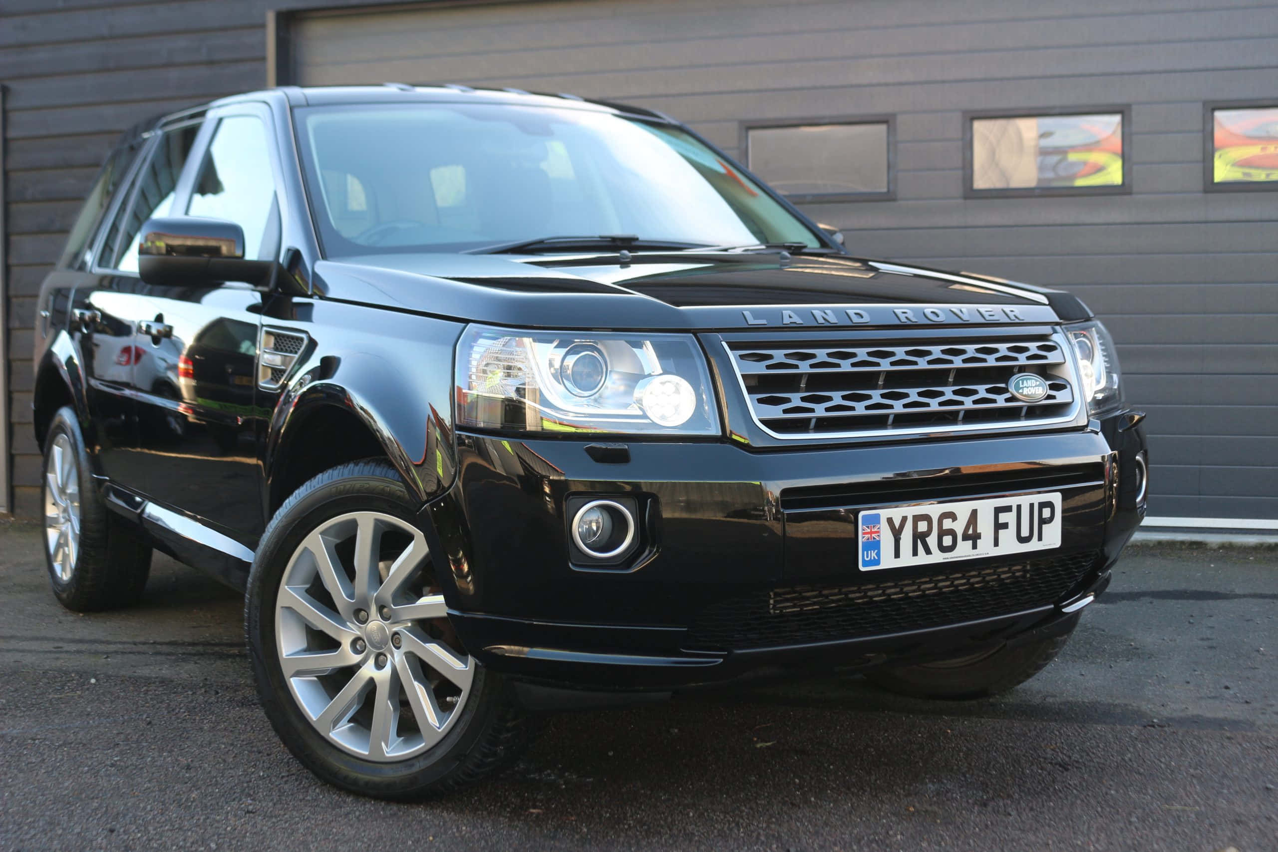 Land Rover Freelander 桌布 壁紙 — 一輛亮黑色Land Rover Freelander 2停泊在現代灰色車庫前，配備反光鍍鉻輪圈。