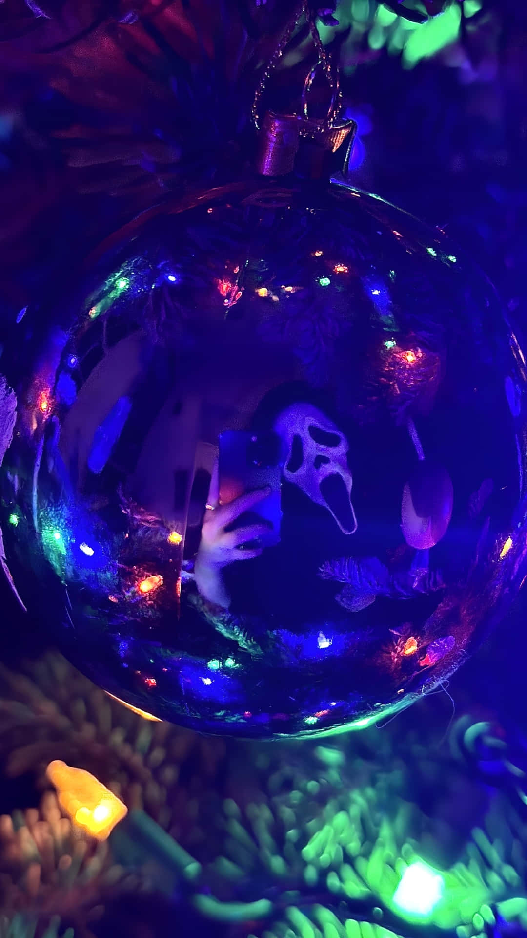  壁紙 — 一個光亮的聖誕裝飾反射出一個人在昏暗的樹中手持帶有Ghostface面具的電話。