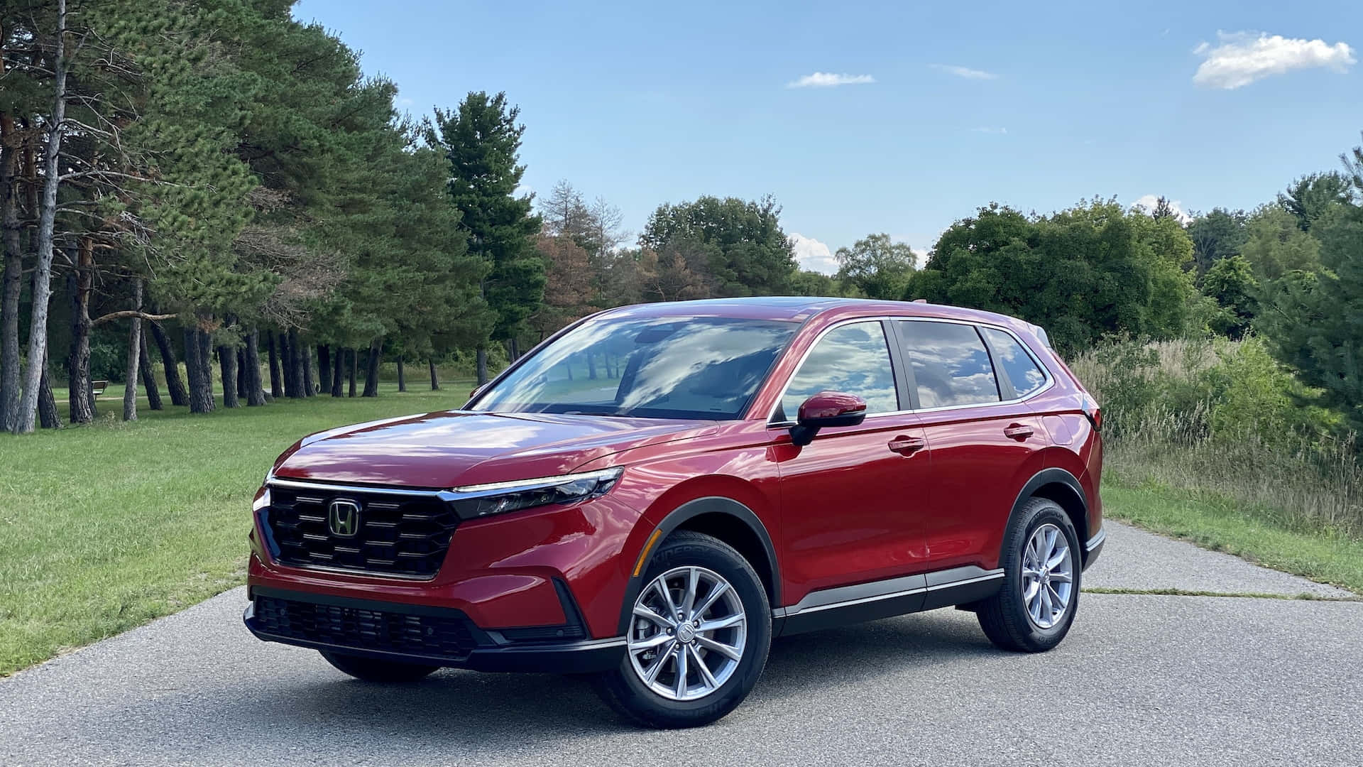 Honda Cr-v 桌布 壁紙 — 一架亮麗的紅色本田SUV停泊在鋪設的道路上，周圍是高聳的樹木和綠草，在晴朗的藍天下。