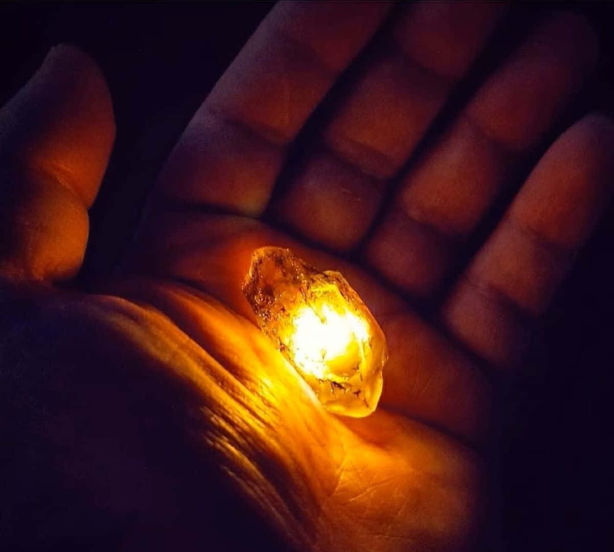  壁紙 — 一顆發光的橙色水晶放在張開的手掌上，在黑暗的背景中投射出溫暖的光芒。