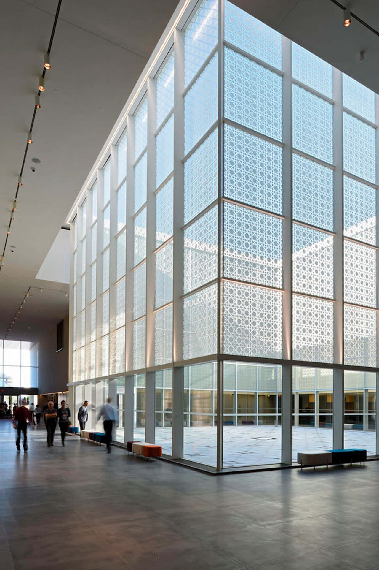 Aga Khan Museum 桌布 壁紙 — 一個宏偉的現代中庭，設有高聳的玻璃牆，呈現複雜的幾何圖案，人們在明亮的自然光下行走。