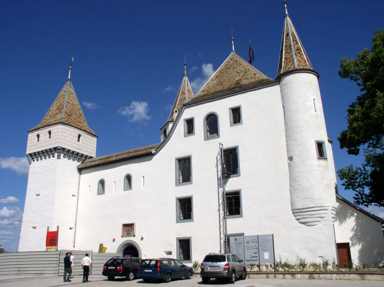 Nyon Switzerland 桌布 壁紙 — 一座宏偉的白色城堡，擁有圓錐形屋頂和石塔，矗立在晴朗的藍天白雲下。