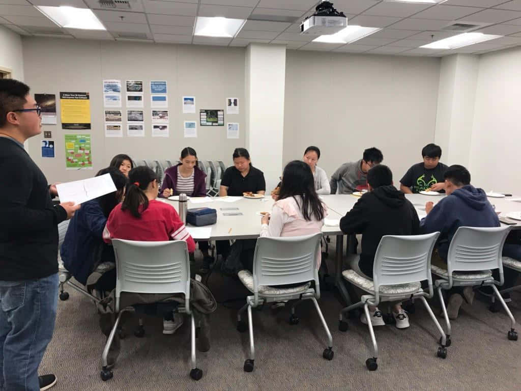  壁紙 — 一群人聚集在現代辦公室房間的會議桌旁，房間內有頭頂照明和牆上海報。