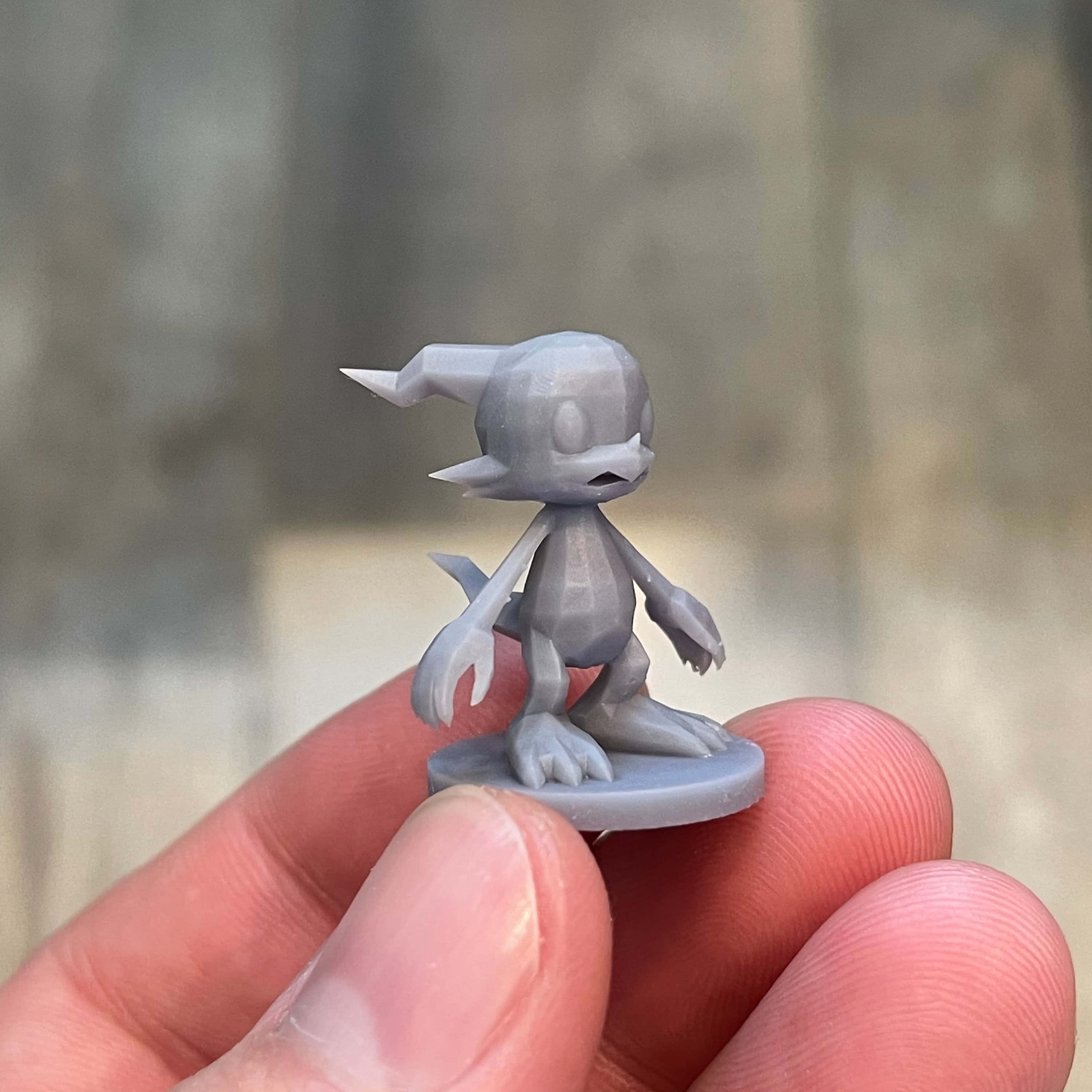Veemon 桌布 壁紙 — 一隻手拿著一個細小灰色3D打印的風格化生物公仔，有尖耳朵和爪子。