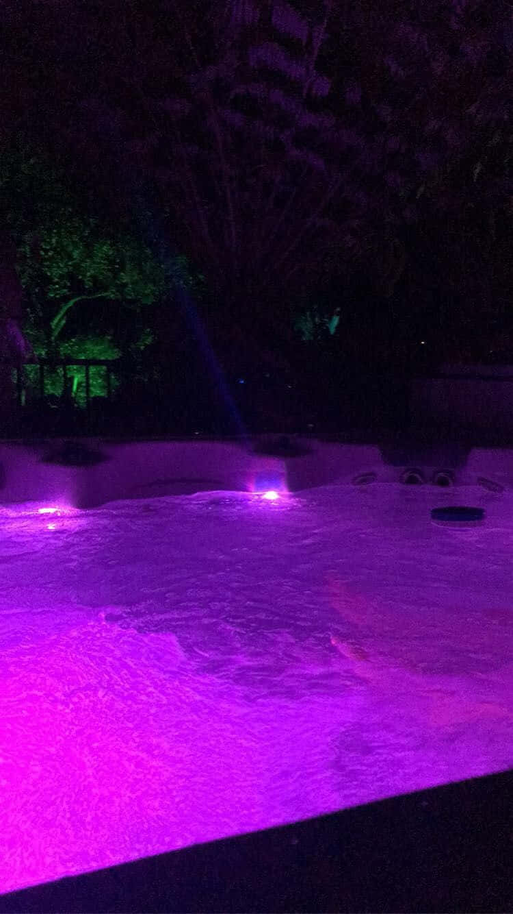  壁紙 — 一個在黑暗夜空下被樹木環繞、散發著鮮豔紫色光芒的熱水浴缸。