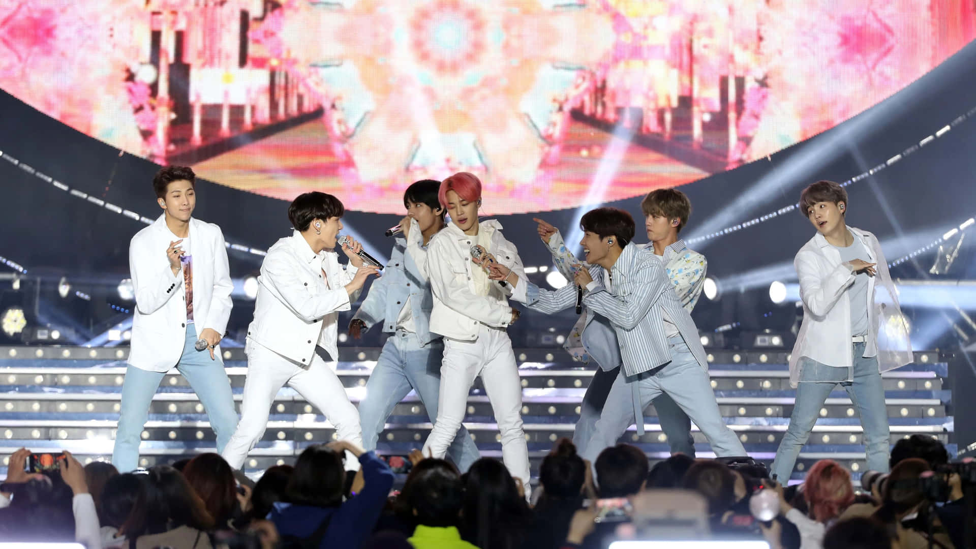 K-pop團體在舞台上表演，燈光明亮，前景有觀眾。