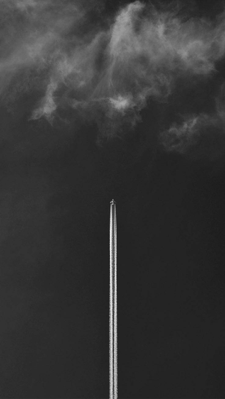 一架飛機在高空飛行，在多雲的天空中留下一條長長的白線。