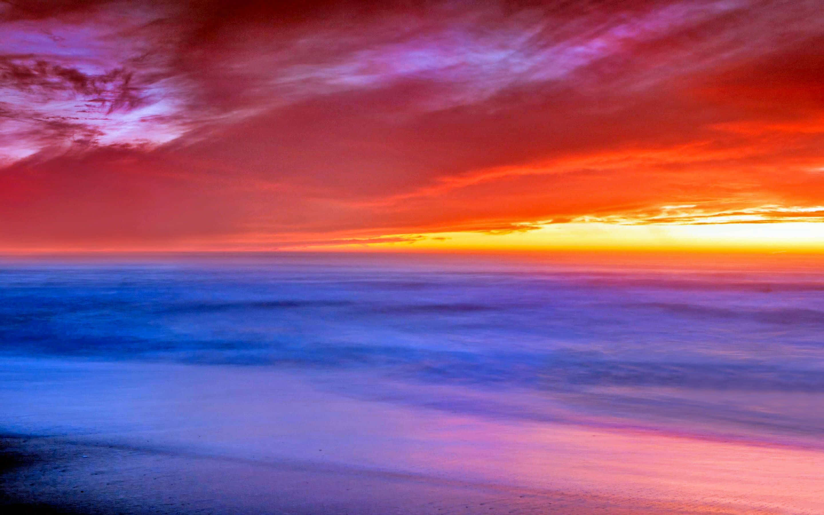 Colorful Sunset 桌布 壁紙 — 日落時分長曝光的海景，火紅橙色和紫色的雲彩映照在平滑的藍色水面上。