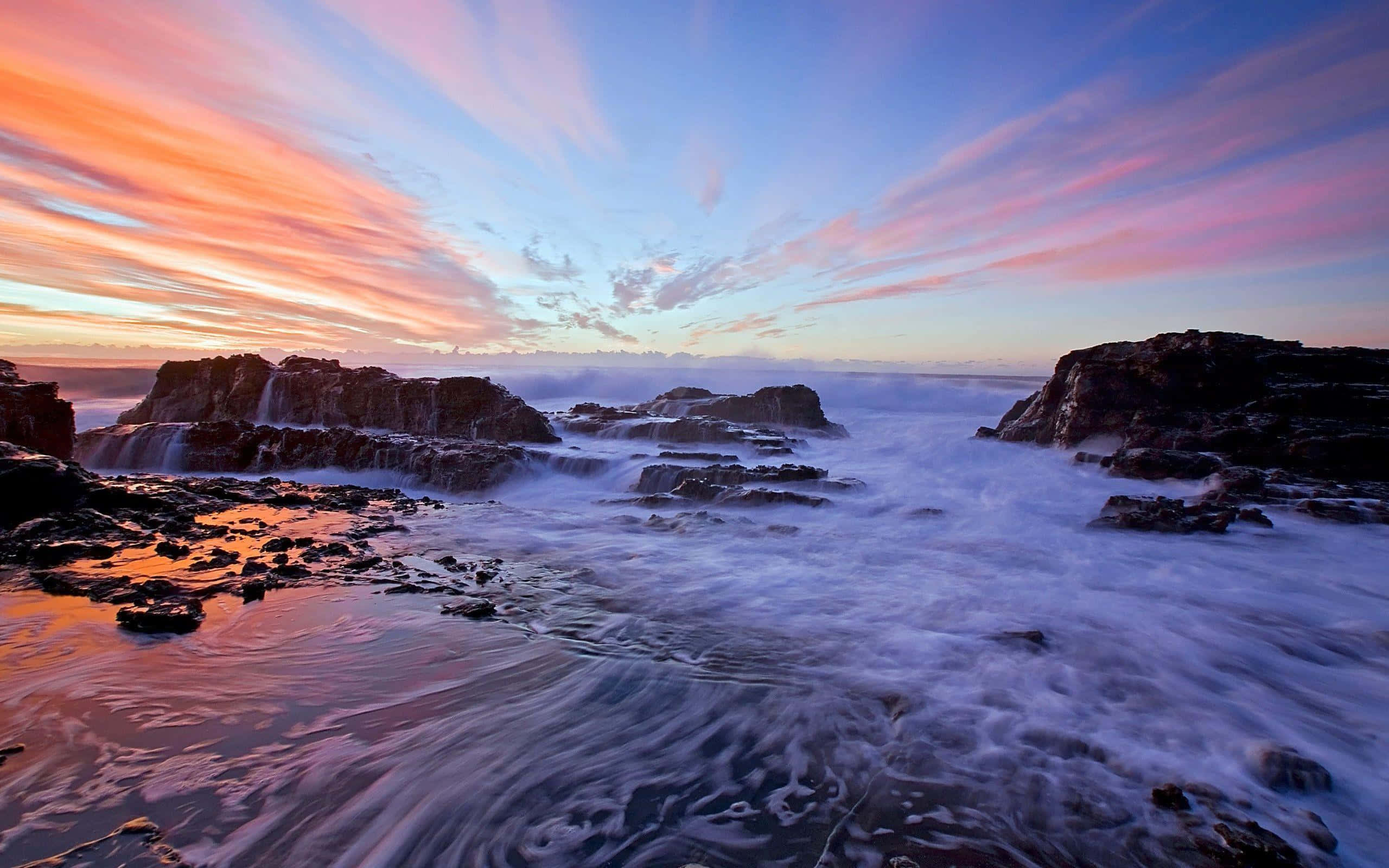 Beautiful Ocean 桌布 壁紙 — 日落時分的長時間曝光海景，鮮豔的粉紅色和橙色雲彩在深色岩石和泡沫白色水面上劃過。