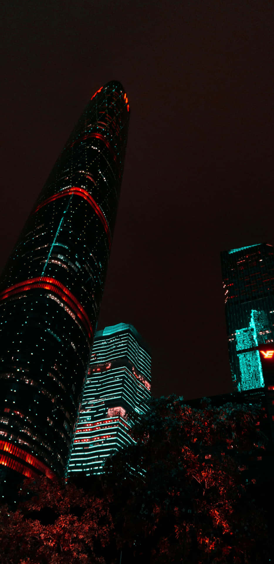  壁紙 — 低角度夜攝，高聳摩天大樓在黑暗天空中閃爍紅與青綠燈光。