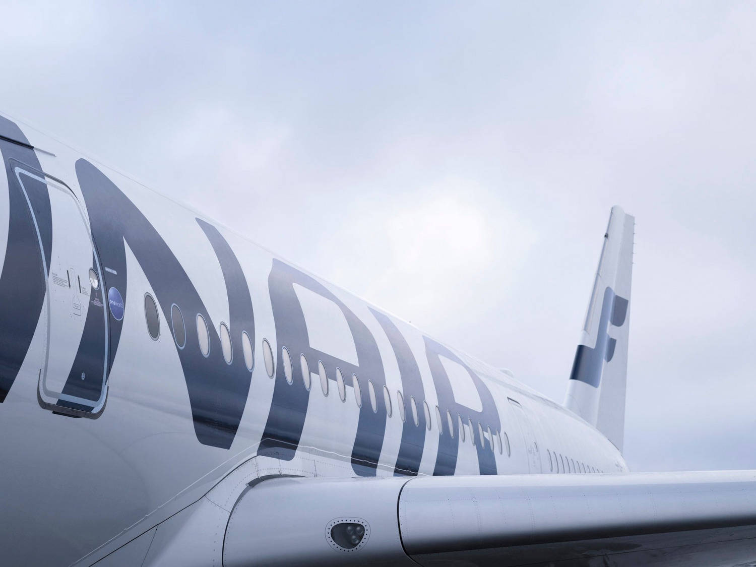 芬蘭航空垂直尾翼特寫 壁紙 — 卡塔爾航空飛機機身嘅低角度視圖，背景係明亮嘅多雲天空。