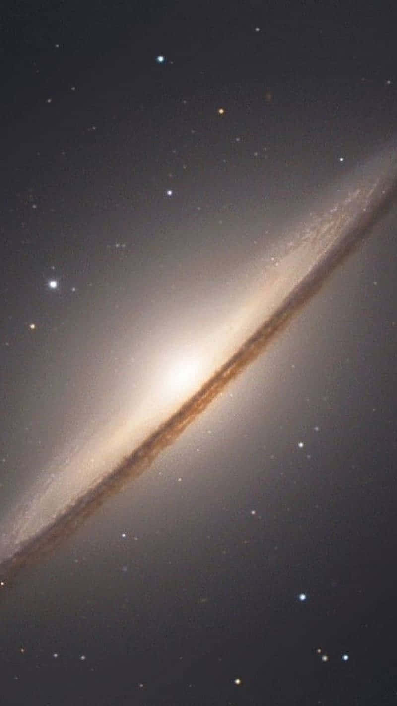  壁紙 — 一個明亮的螺旋星系斜向穿過星場，帶有發光的塵埃帶和明亮的核心。