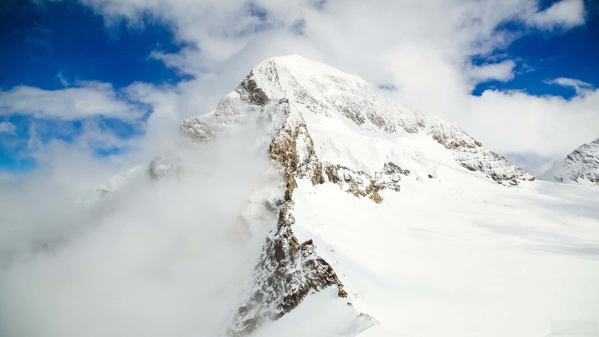 雪山頂峰聳立於雲層之上，藍天為背景