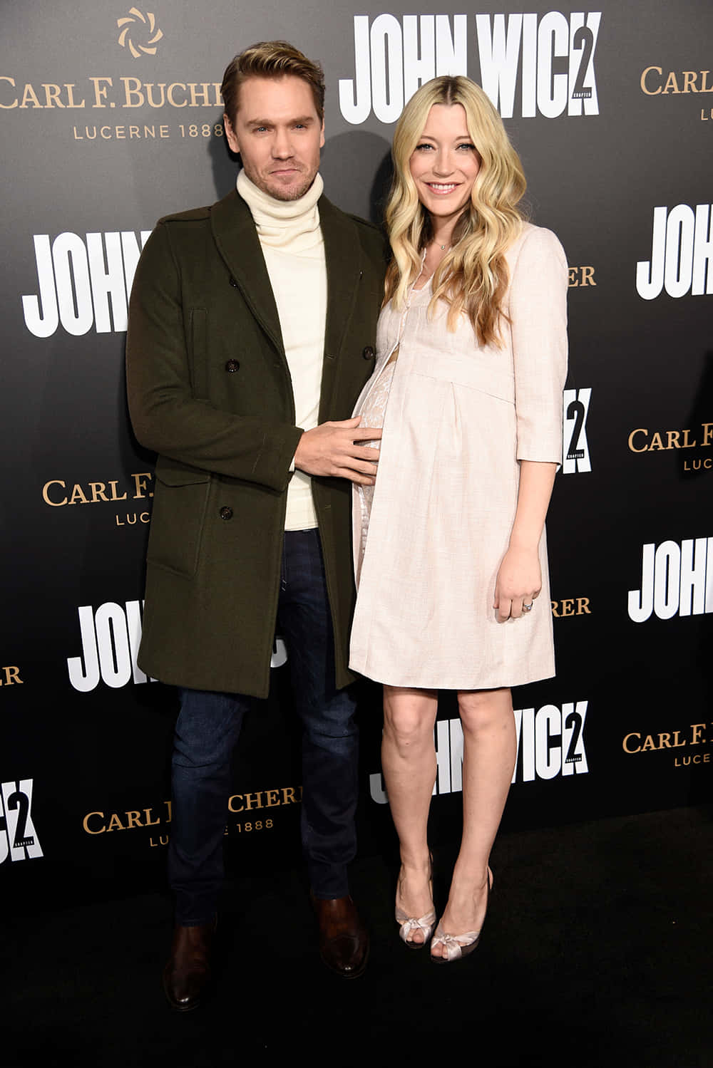 Sarah Roemer 桌布 壁紙 — 一名男子和一名孕婦在約翰威克2首映活動中一起擺姿勢，背景帶有品牌標誌。