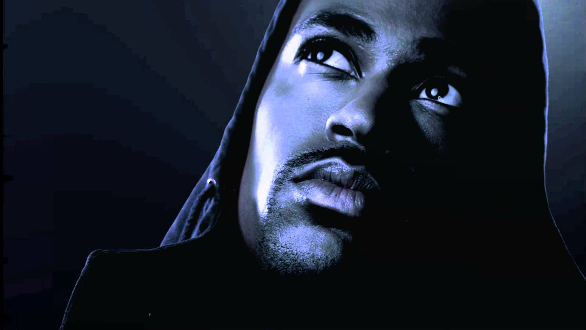 Big Sean 美學造型 壁紙 — 一個穿著深色連帽衫的男人，在黑色背景上戲劇性的藍色燈光下，用強烈的眼神向上凝視。