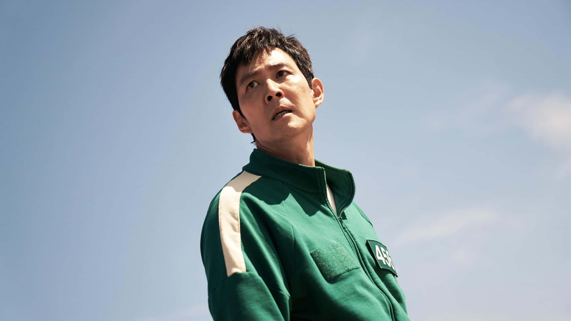  壁紙 — 一名身穿綠色號碼運動服的男子，表情嚴肅地仰望清澈的藍天。