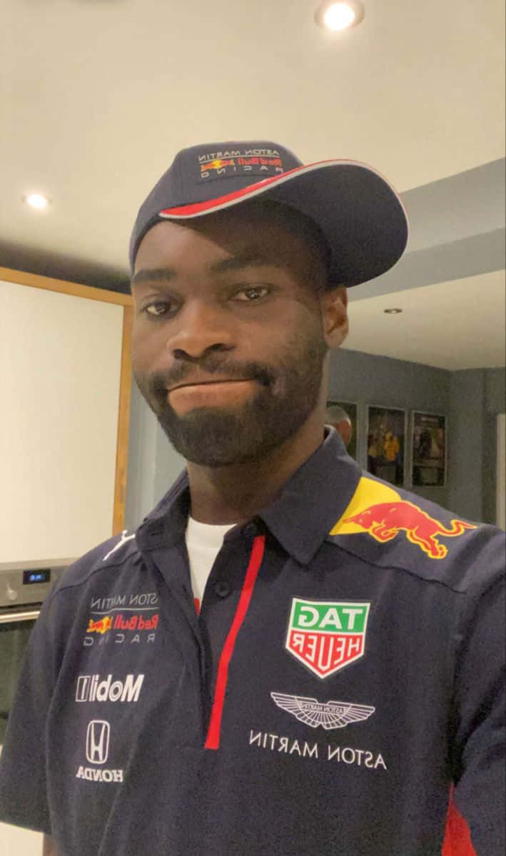  壁紙 — 一名身穿Red Bull Racing車隊外套和帽子的男士在天花板燈光下於室內輕柔微笑。