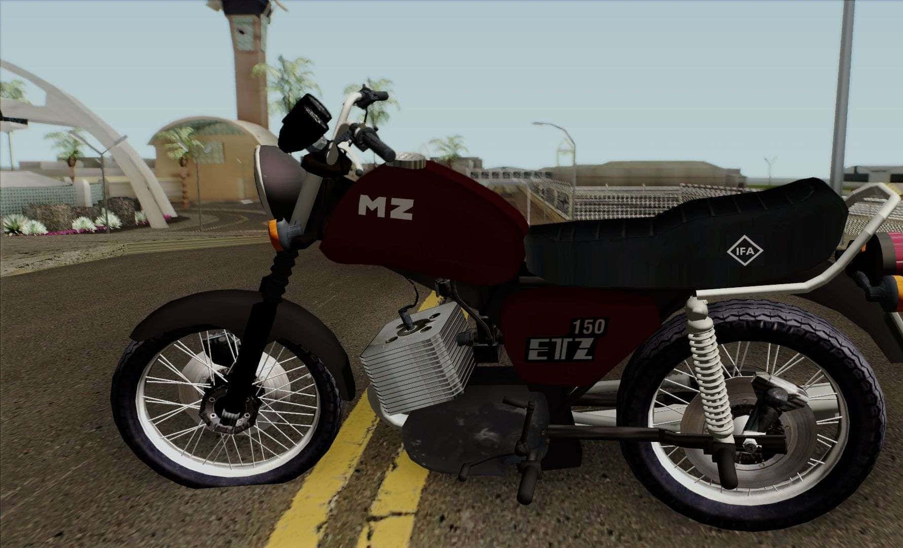 Mz Motorcycle 桌布 壁紙 — 一輛栗色和黑色的150cc電單車，配有白色鋼絲輪，停泊在現代拱門和棕櫚樹附近的鋪砌道路上。