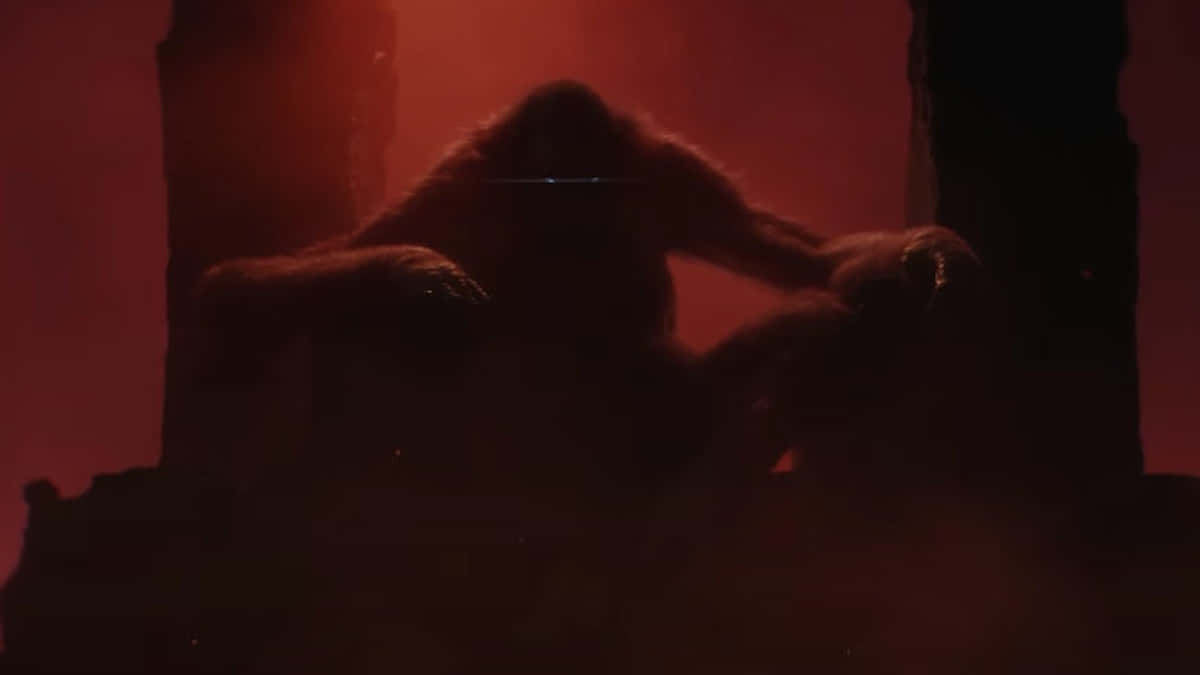 Godzilla X Kong The New Empire 桌布 壁紙 — 一隻巨大的猿坐在廢棄的石結構中，以剪影形式映襯著發光的紅色霧氣。