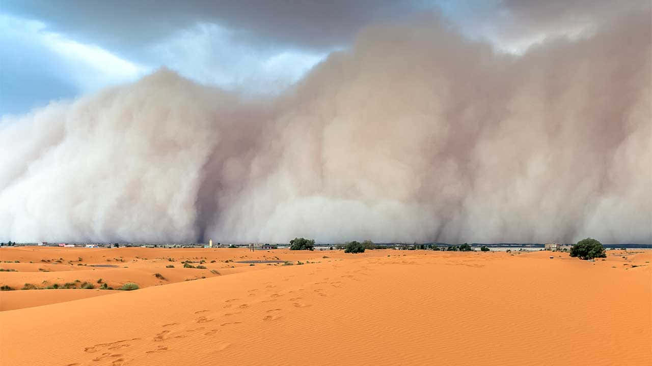  壁紙 — 一場巨大的沙塵暴在戲劇性的多雲天空下席捲廣闊的橙色沙漠景觀。