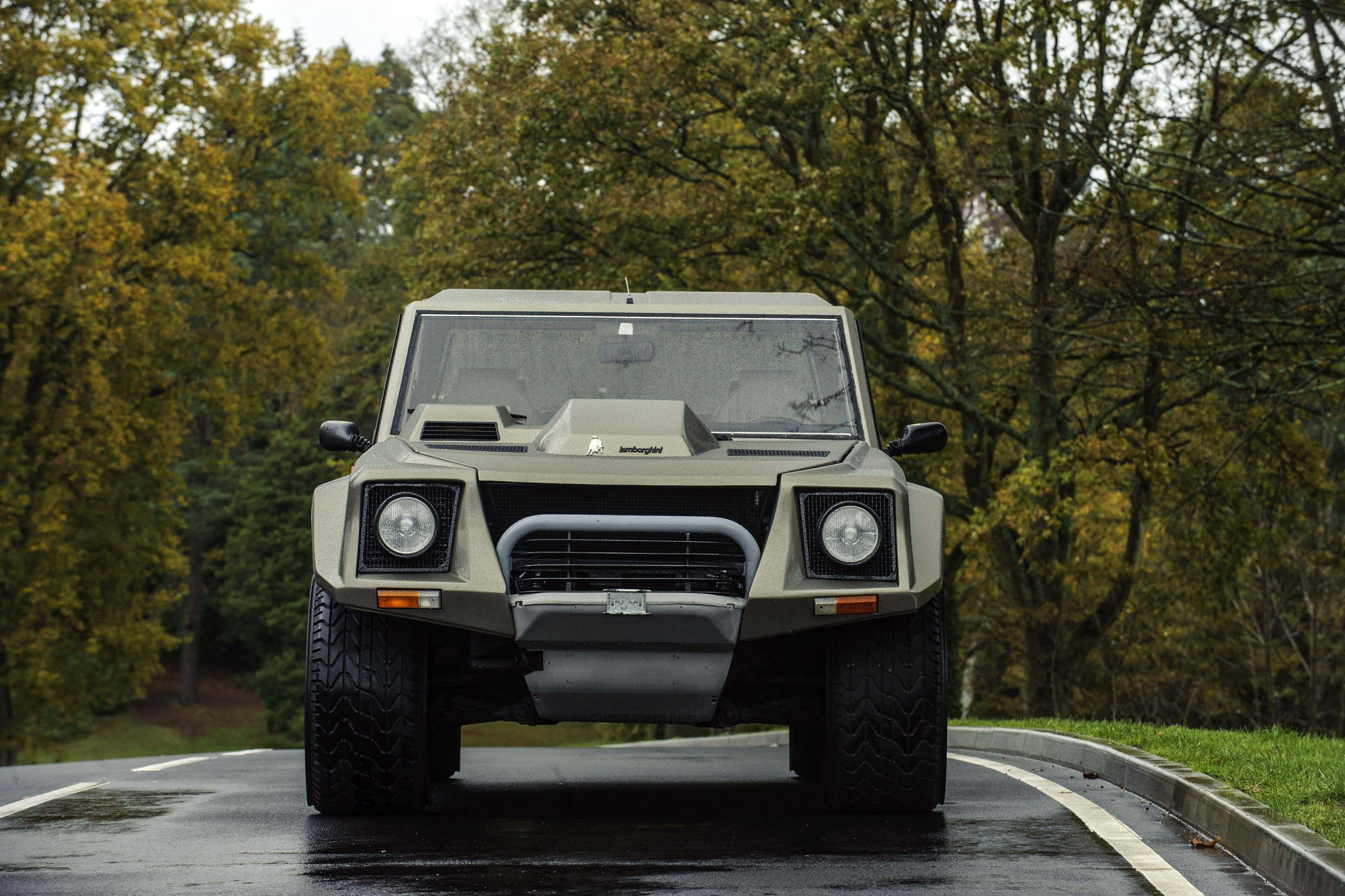 Lamborghini Lm002 桌布 壁紙 — 一輛啞光米色的林寶堅尼LM002大膽地停在濕潤的森林道路上，周圍是秋天的樹木。