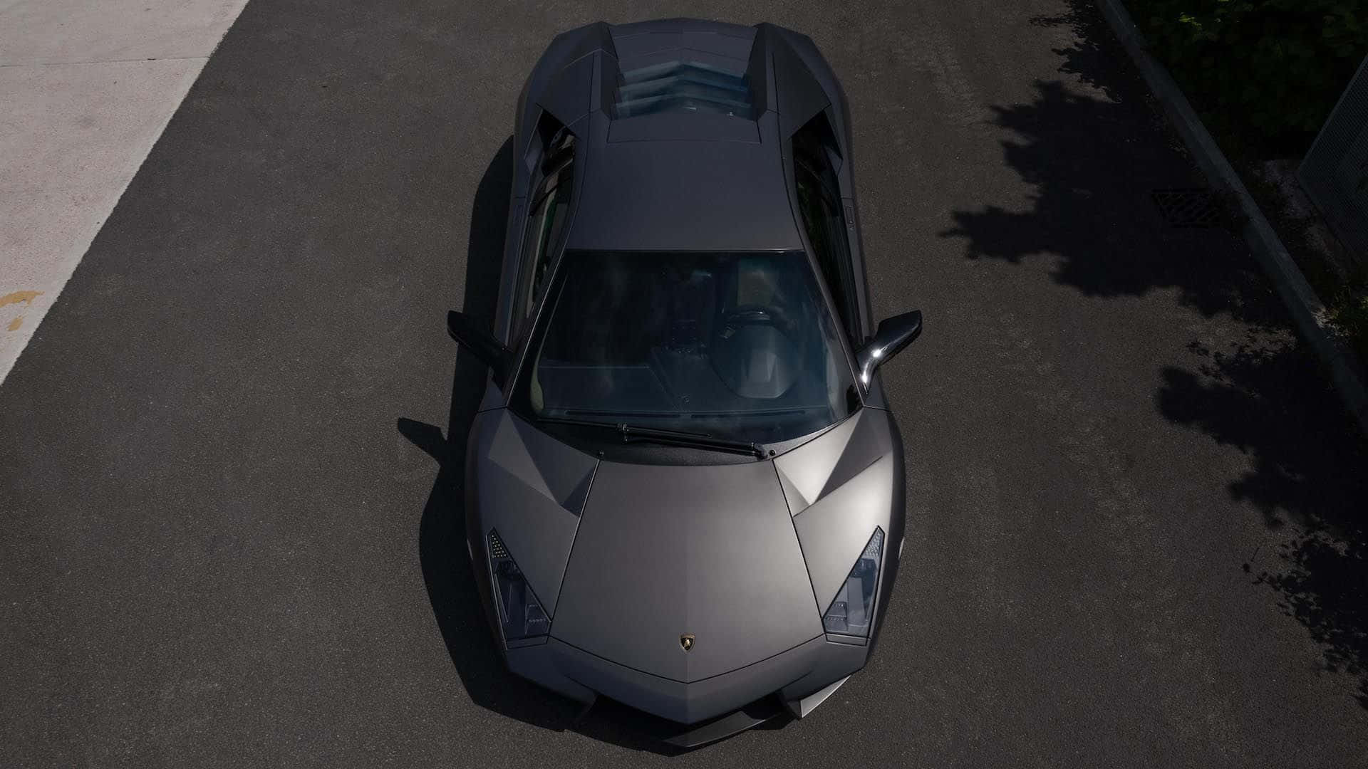 Lamborghini Reventón 桌布 壁紙 — 一輛啞光灰色的林寶堅尼 Aventador 在日間停泊在瀝青路上，帶有樹影。