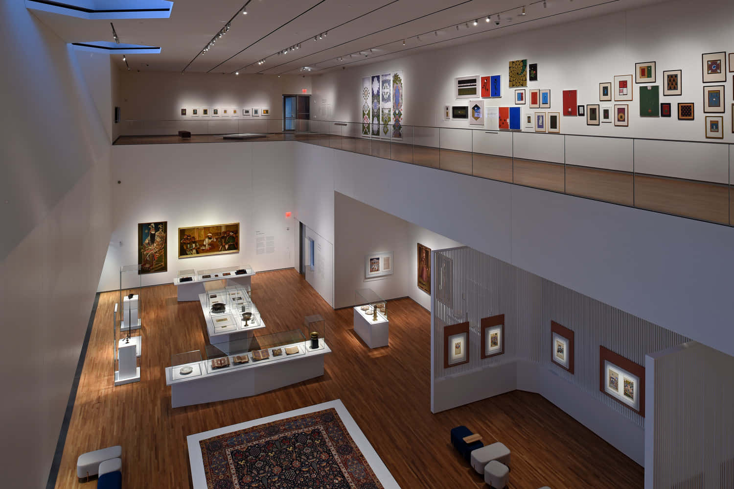 Aga Khan Museum 桌布 壁紙 — 一個現代藝術畫廊，舖有木地板、玻璃欄杆，白色牆壁上在明亮射燈下展示畫作。