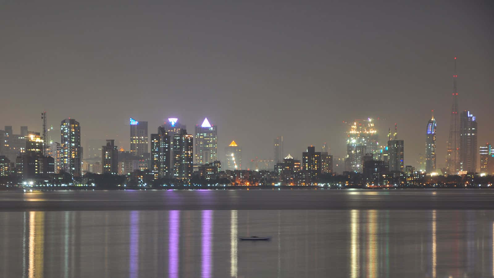 夜晚城市天際線，發光的建築物倒映在平靜的水面上，還有一艘小船。
