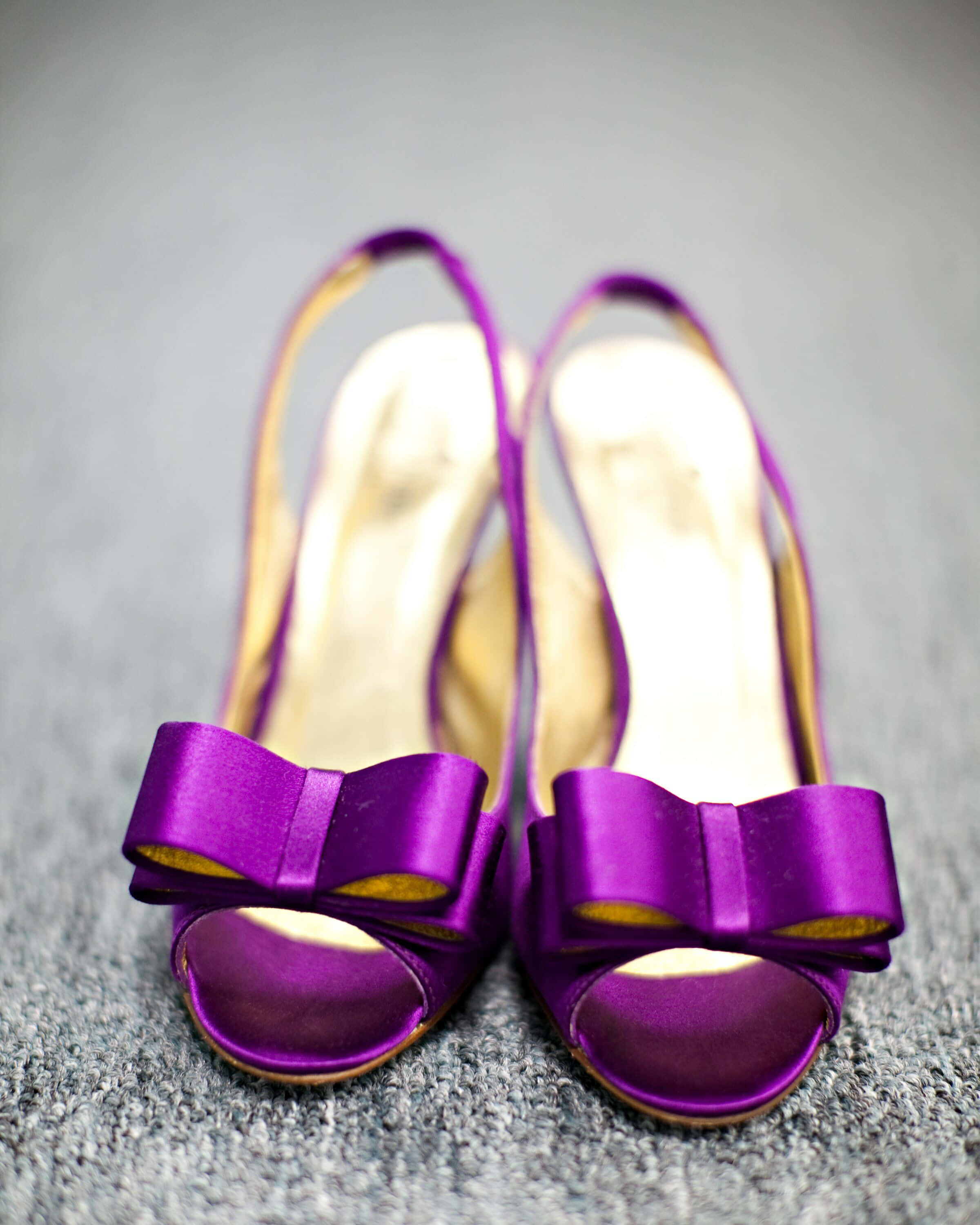Purple Shoes 桌布 壁紙 — 一對充滿活力的紫色緞面高跟鞋，帶有金色飾邊和蝴蝶結，放在灰色紋理地毯上。