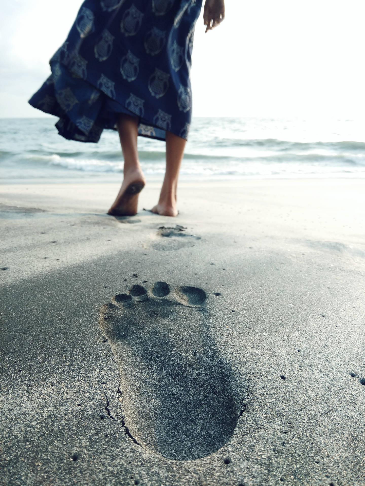 海灘濕沙上一個女人的赤腳腳印，伴隨著海浪。