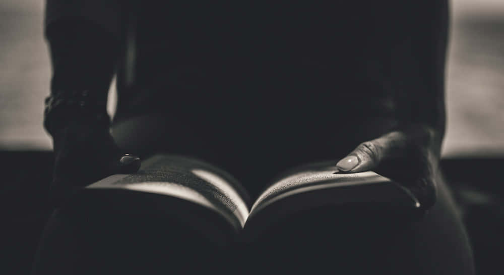  壁紙 — 一個人的雙手輕輕捧著一本打開的書，處於昏暗、陰鬱的黑白環境中。