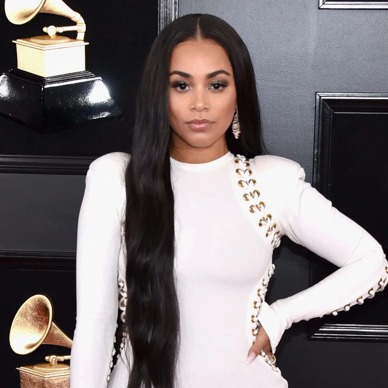 Lauren London 桌布 壁紙 — 一位身穿白色禮服、飾有金色裝飾的優雅女性，自信地站在黑色背景前的格林美獎座旁。
