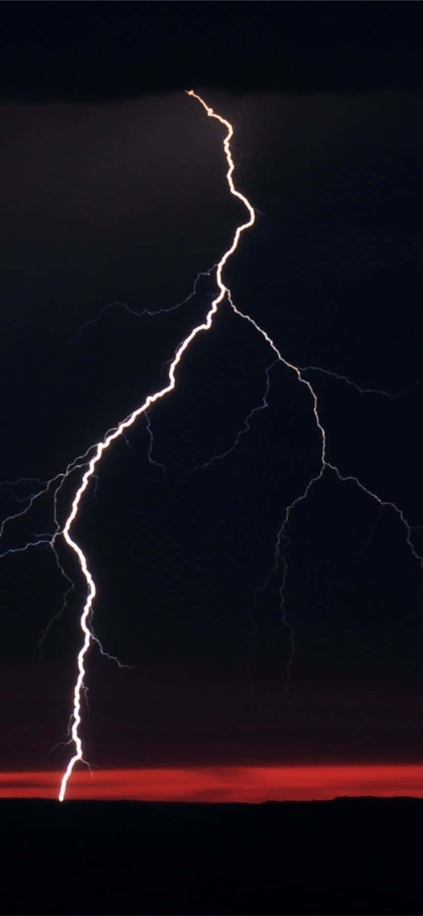 Lightning iPhone 桌布 壁紙 — 一道強勁的鋸齒狀閃電在黑暗的天空中分叉，下方是火紅的地平線。