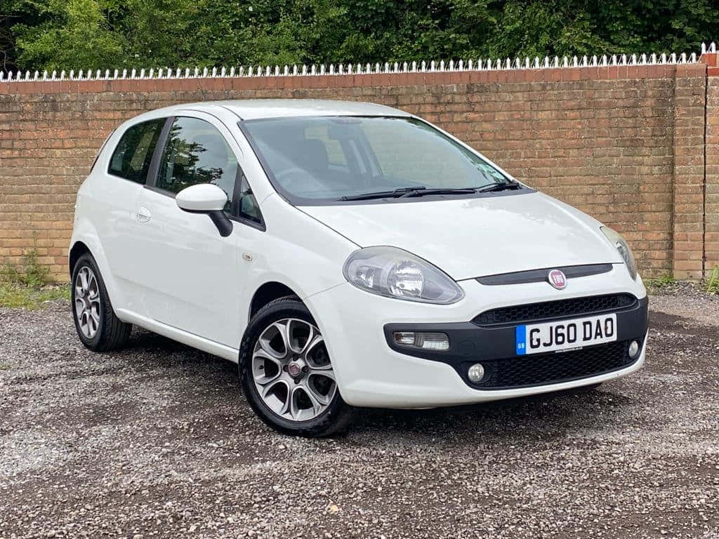 Fiat Punto 桌布 壁紙 — 一架純白色嘅Fiat Punto泊喺磚牆旁邊嘅碎石上，上面有綠色樹葉。