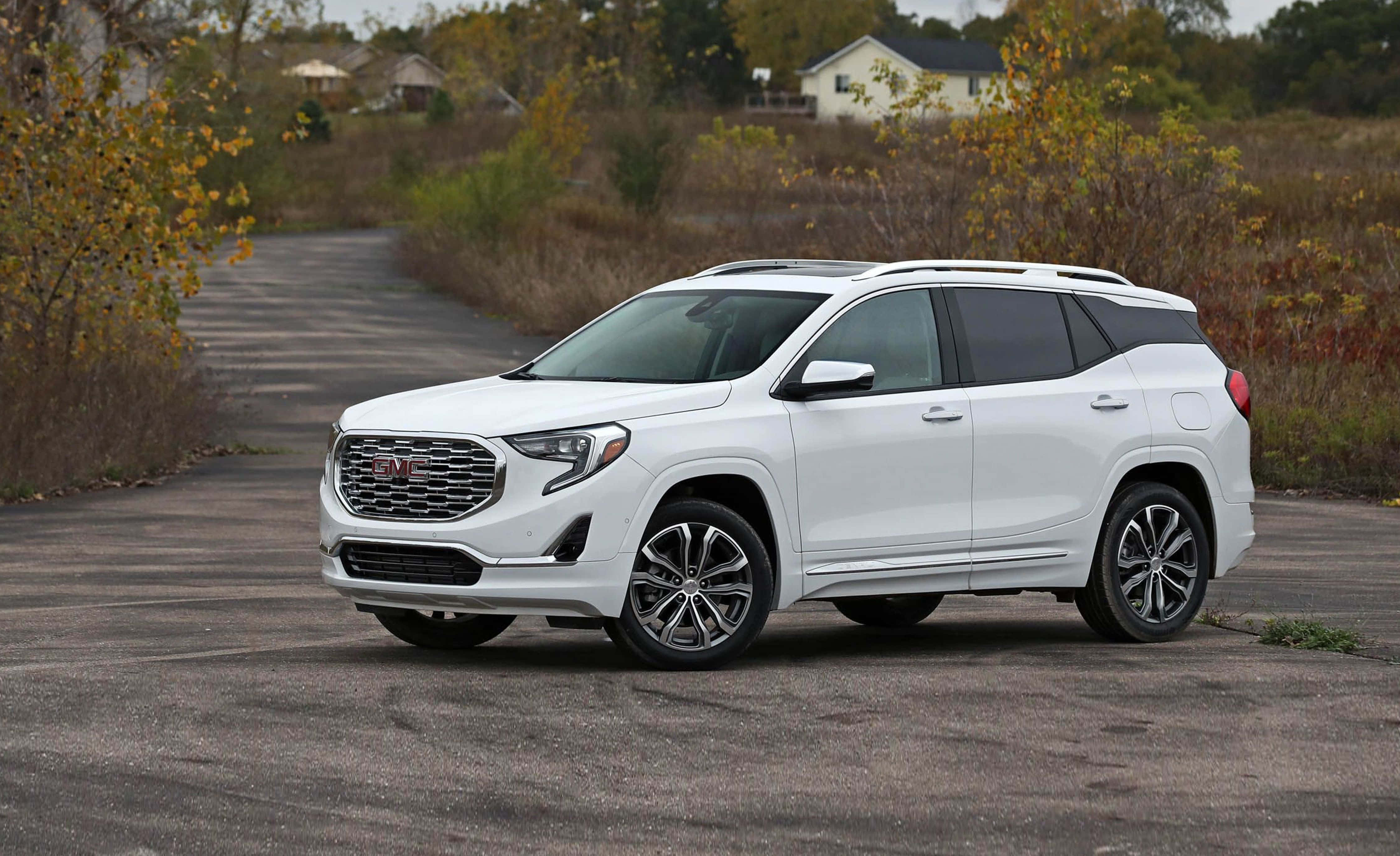 Gmc Terrain 桌布 壁紙 — 一輛純白色的GMC Terrain SUV停泊在碎石車道上，周圍環繞著秋葉和遠處的房屋。