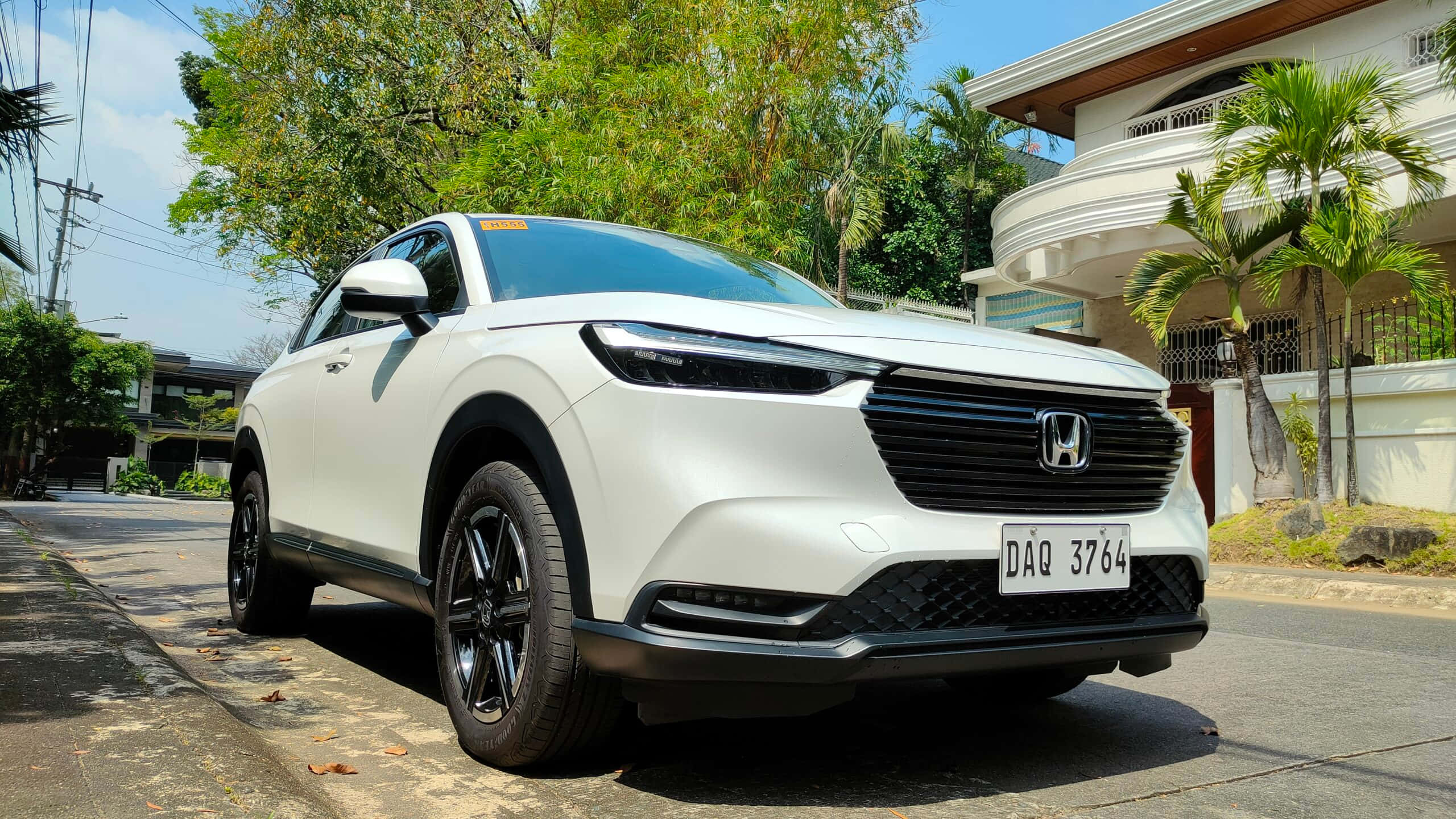 Honda Hr-v 桌布 壁紙 — 一輛純白色的本田SUV停泊在陽光普照的住宅街道上，街道兩旁種滿茂密的綠樹，還有一座白色房子。