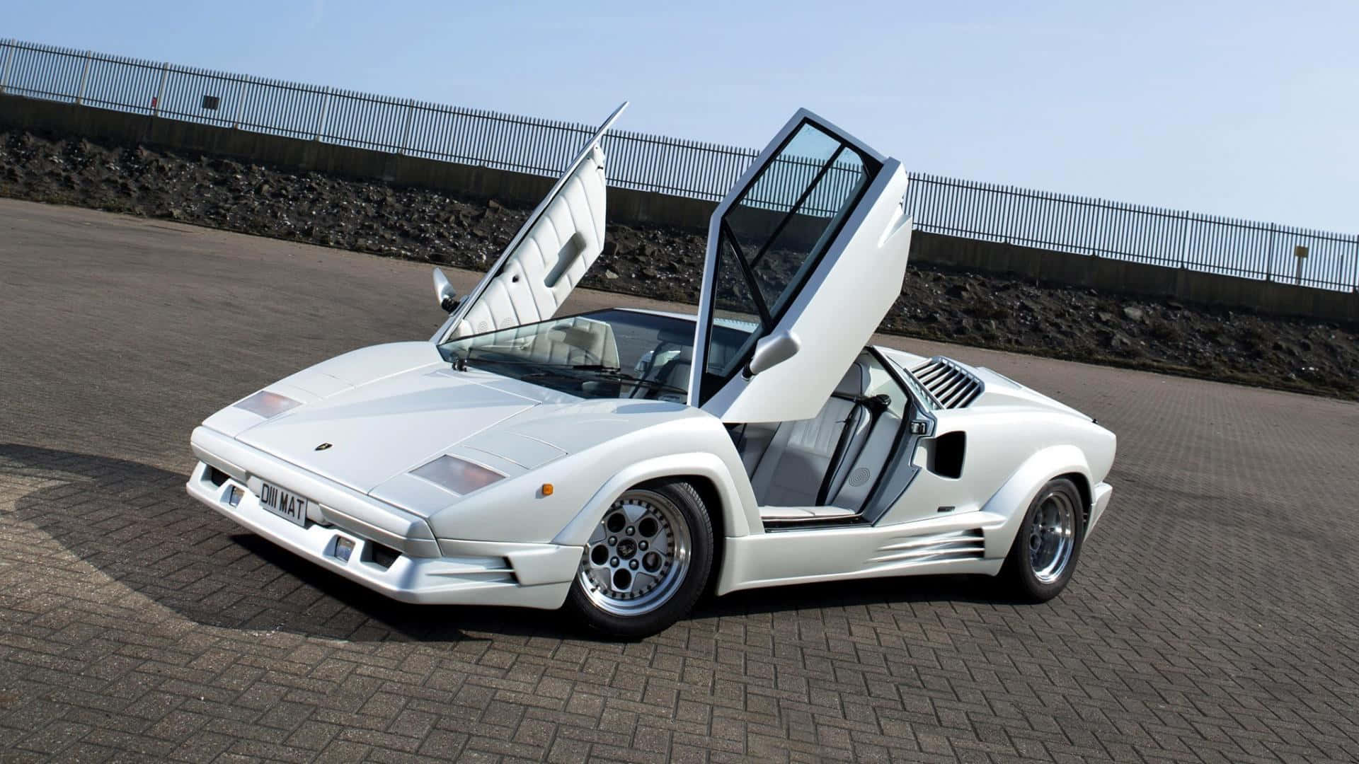 Lamborghini Countach 桌布 壁紙 — 一輛純白色的林寶堅尼Countach，剪刀門打開，停泊在鋪砌路面上，天空晴朗。